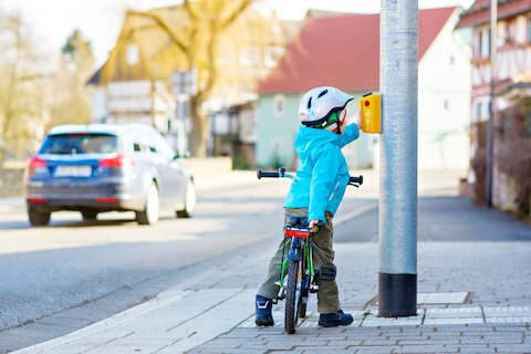 Kind auf Fahrrad steht eigenständig an einer Straße und drückt die Ampel.